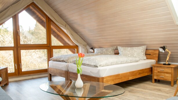 Ein Schlafzimmer mit Holzboden, einem Glastisch, einem Bett mit weißer Bettwäsche und einer Vase mit Blumen.