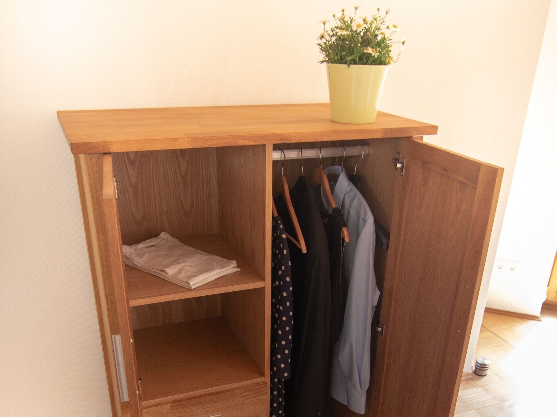 A wooden wardrobe with a shelf, a hanging rod, and a drawer.