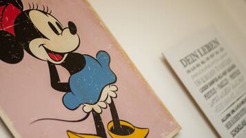 Ilustración de Mickey Mouse sobre un fondo rosa con un menú que detalla precios y servicios.