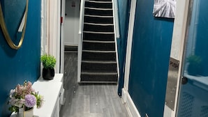 A hallway with blue walls, a white door, a staircase, and a mirror. - Avalon Guest House (Brighton)