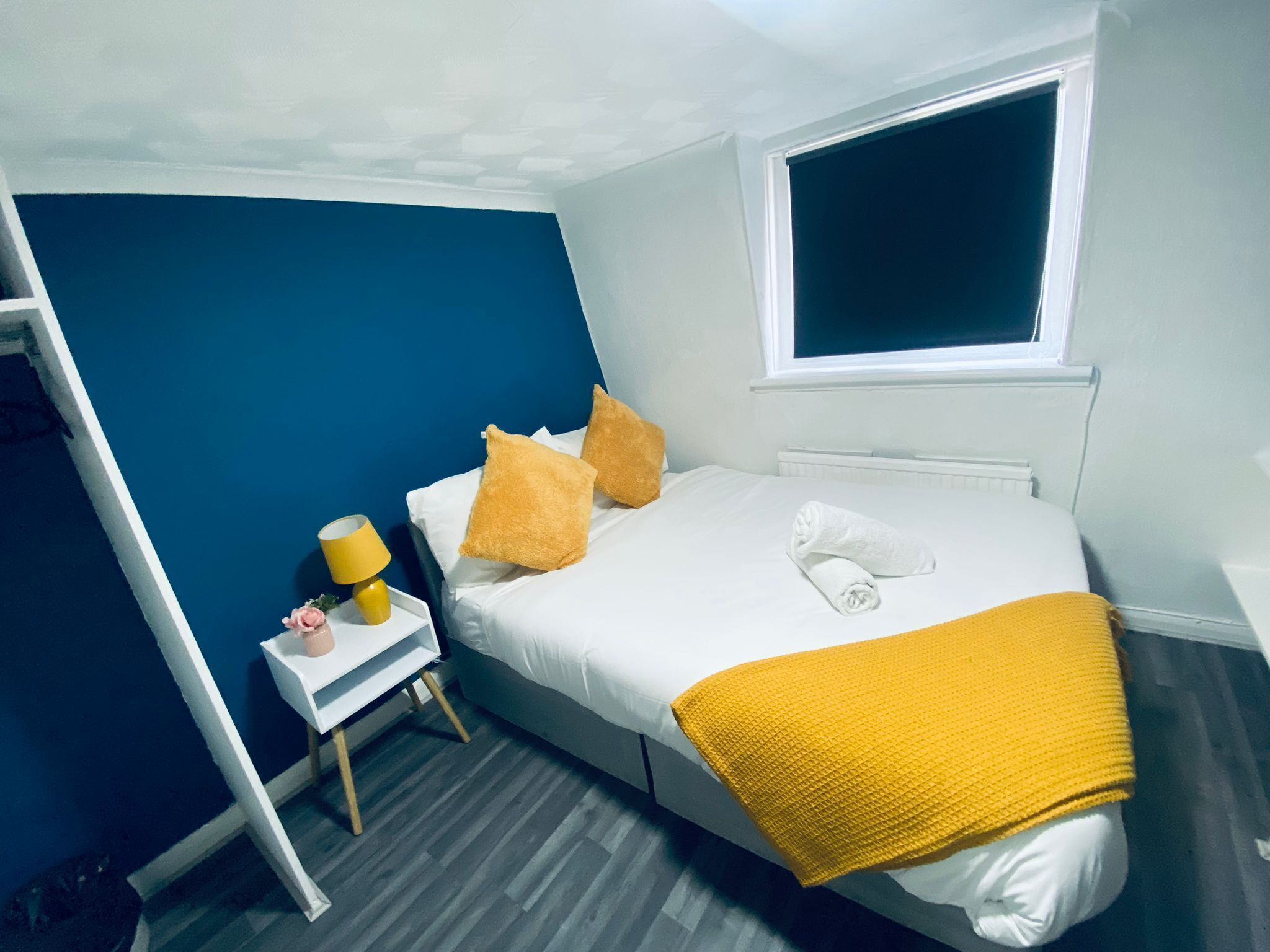 A bedroom with a bed, a nightstand, a window, and a yellow throw blanket.