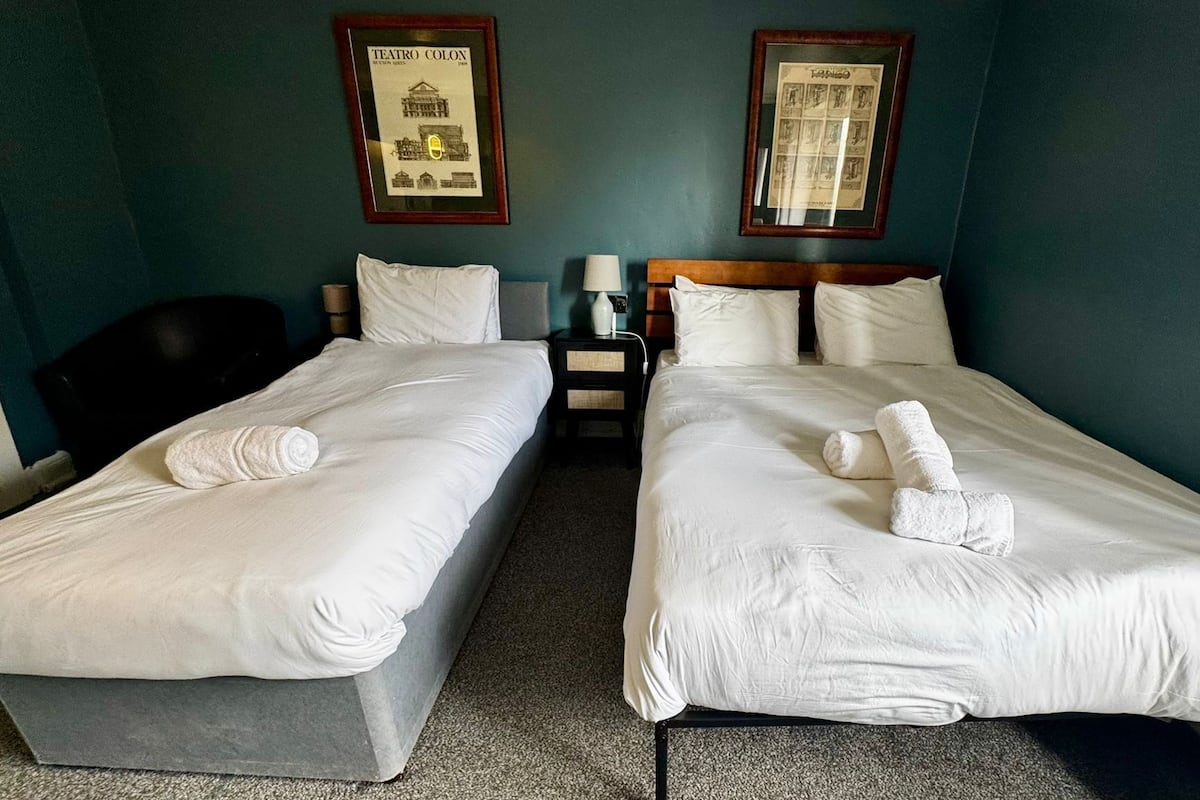A hotel room with two single beds, a nightstand, a lamp, and two framed pictures on the wall.