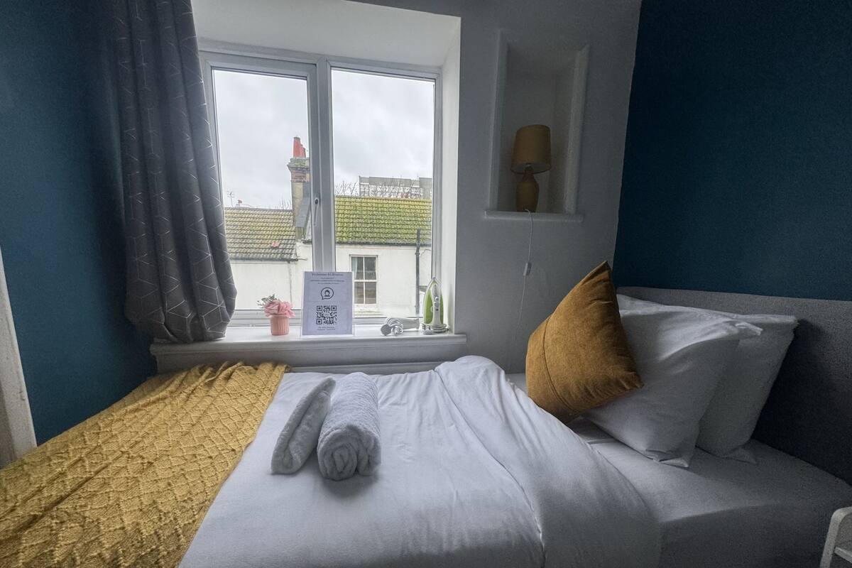 A hotel room with a bed, a window, a lamp, and a sign on the window.