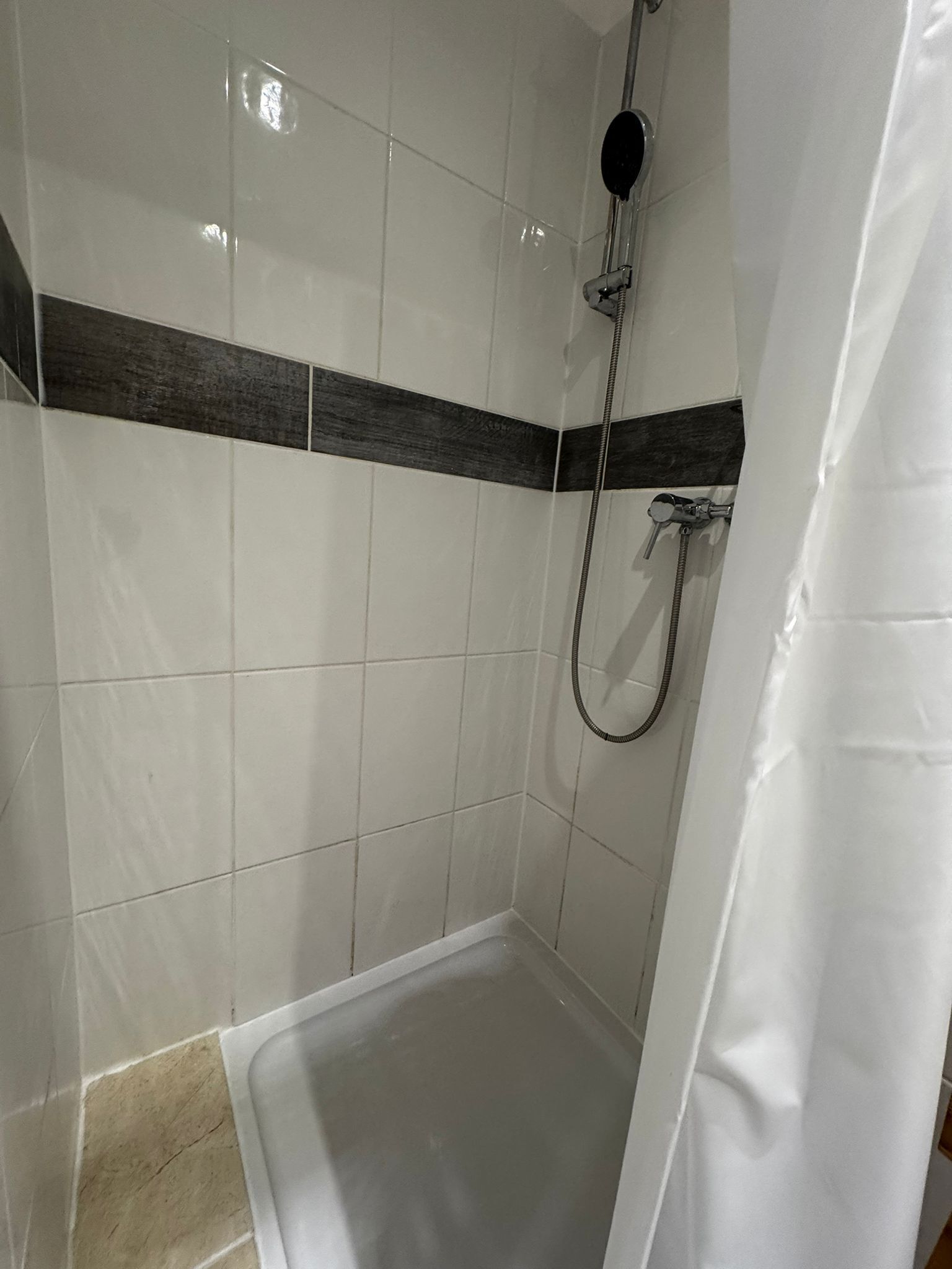 Un espace douche avec des carreaux blancs et une bande horizontale de couleur foncée.