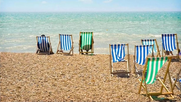 A beach with several striped beach chairs aligned on the sand, facing the ocean. - Avalon Guest House (Brighton)