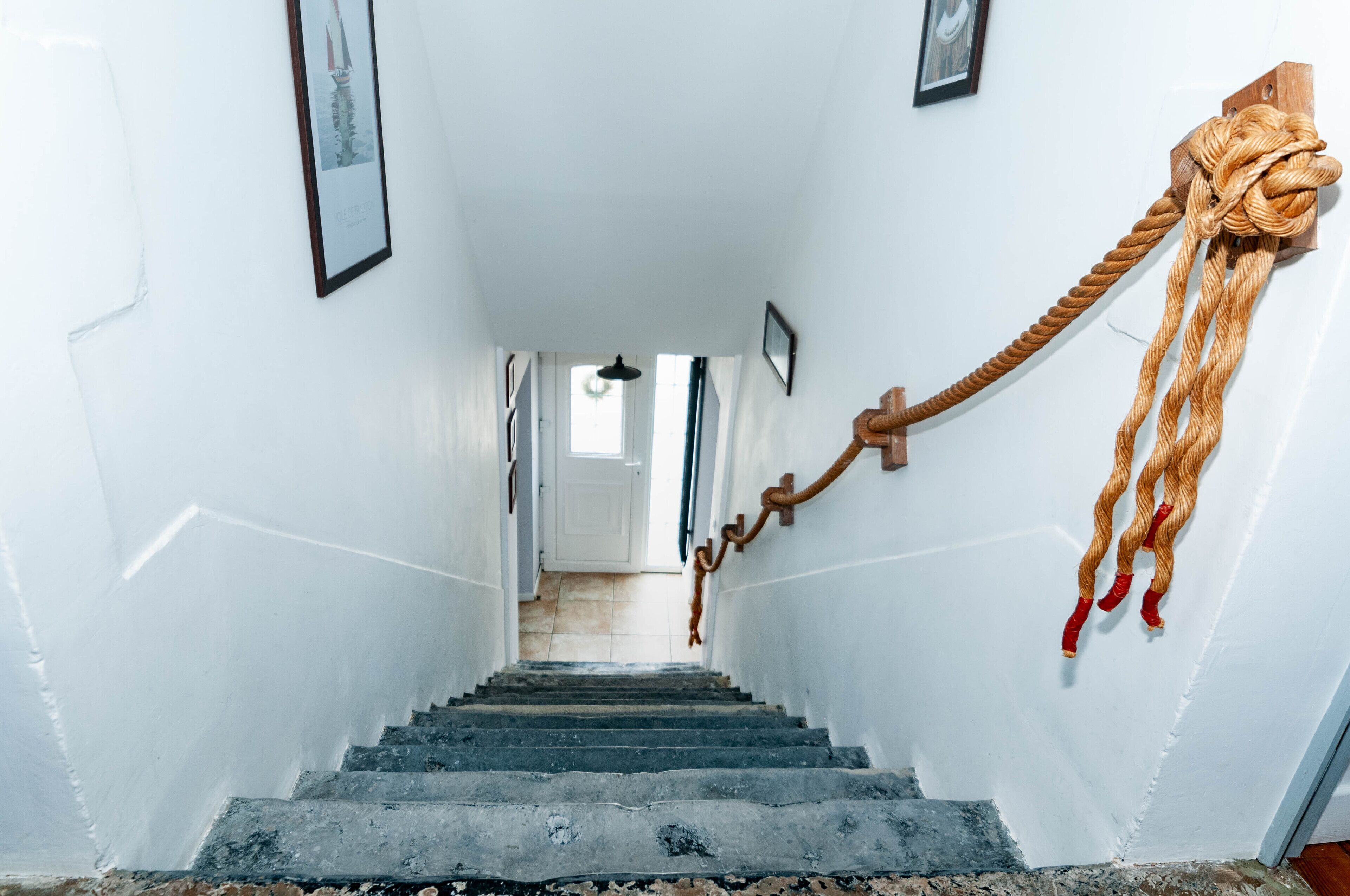 A staircase with a wooden handrail and a rope tied to the wall.