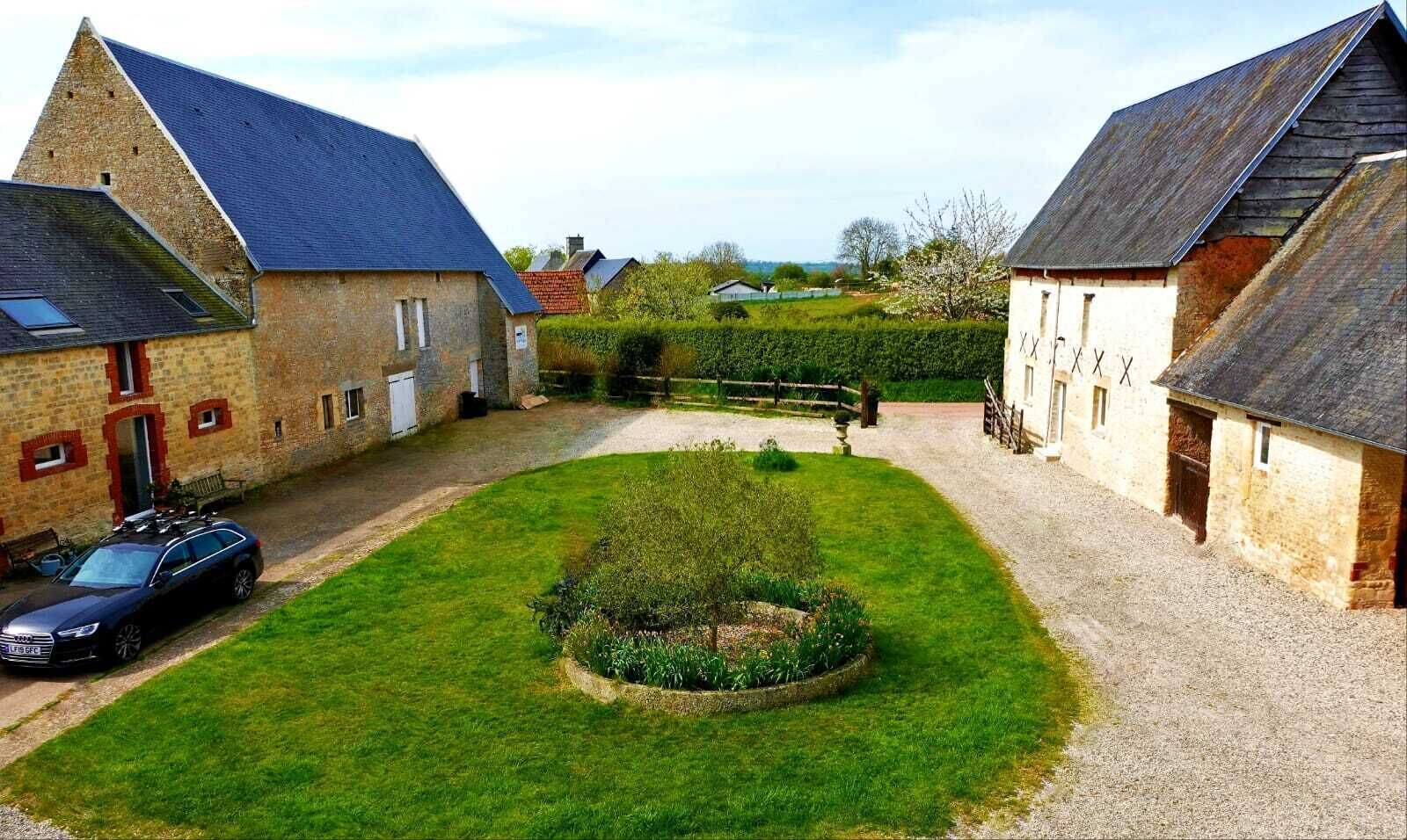 Une cour bordée de bâtiments en pierre, avec une voiture et une pelouse bien entretenue.