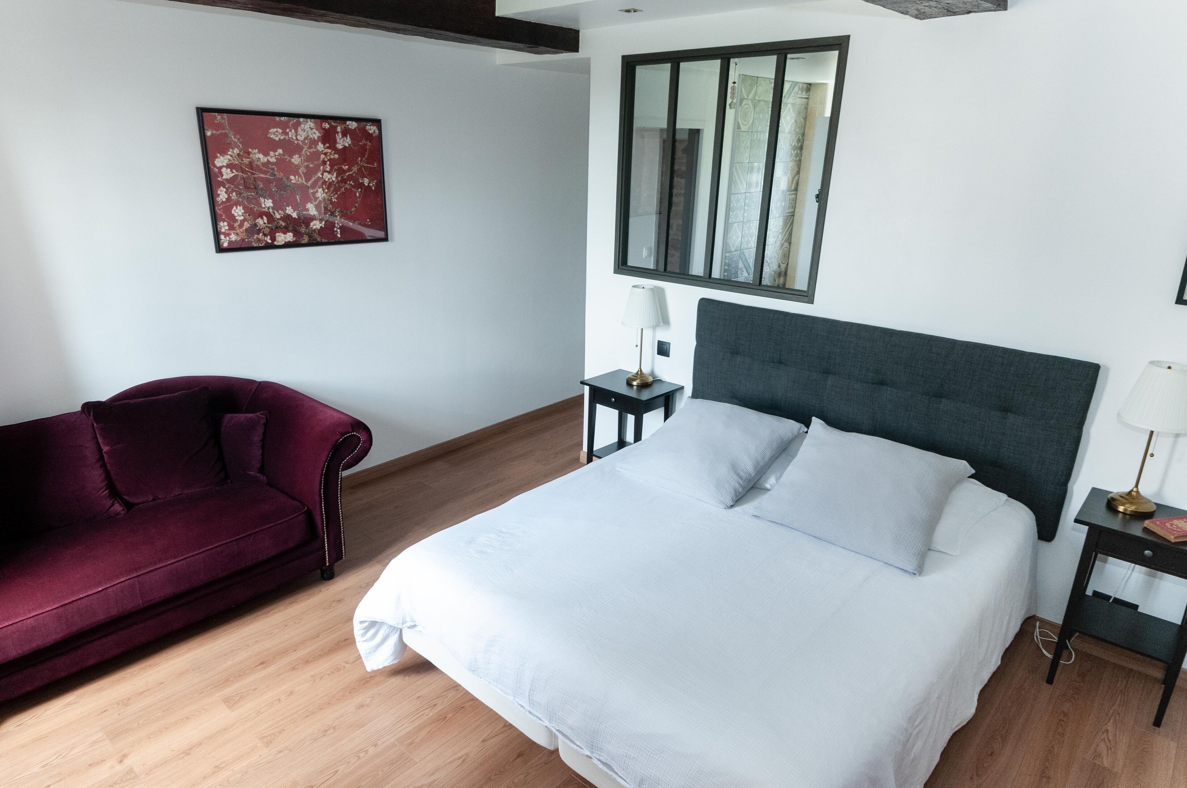 Un dormitorio con una cama, un sofá rojo, una mesita de noche con lámpara y una ventana.