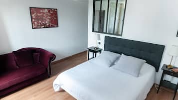 Un dormitorio con una cama, un sofá rojo, una mesita de noche con lámpara y una ventana.