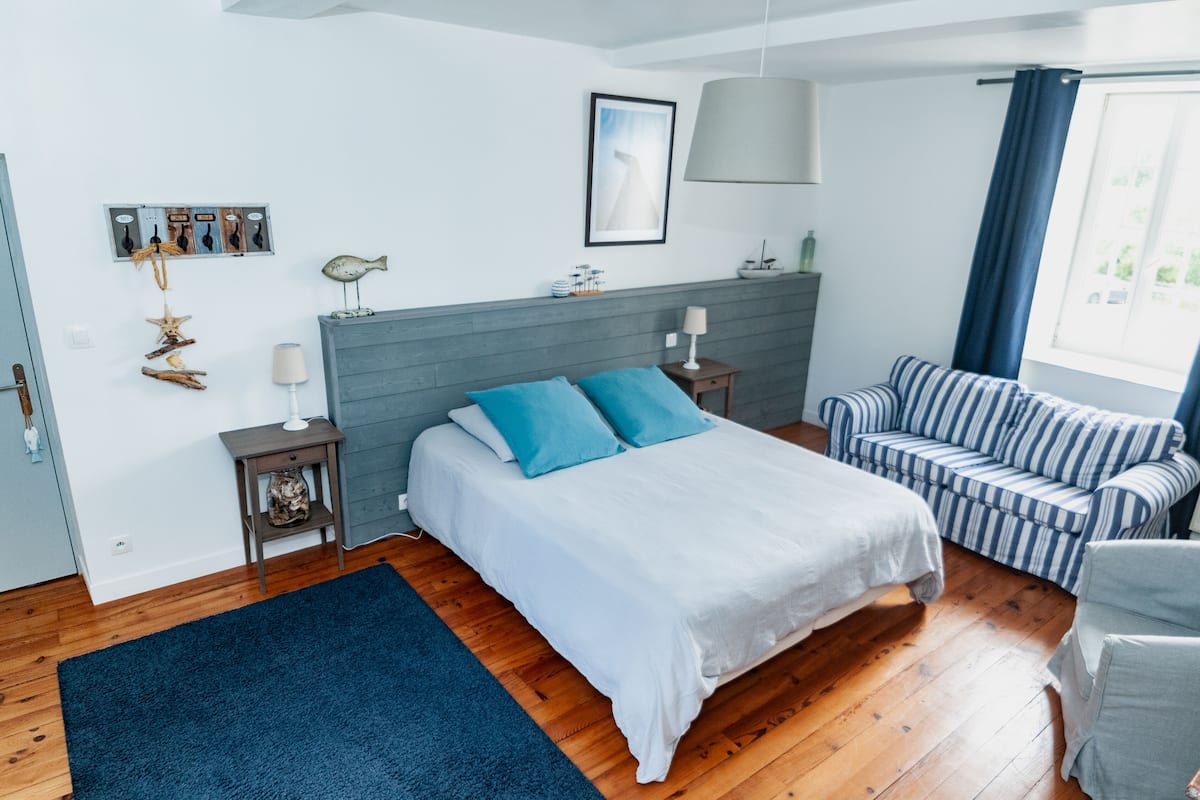 Een slaapkamer met een bed, nachtkastje, lamp, stoel, raam met gordijnen en wanddecoraties, waaronder een vis en zeester.
