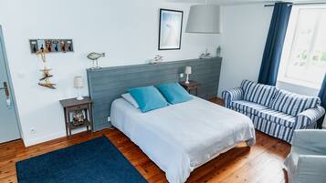 Un dormitorio con cama, mesita de noche, lámpara, silla, ventana con cortinas y adornos en la pared, incluyendo un pez y una estrella de mar.