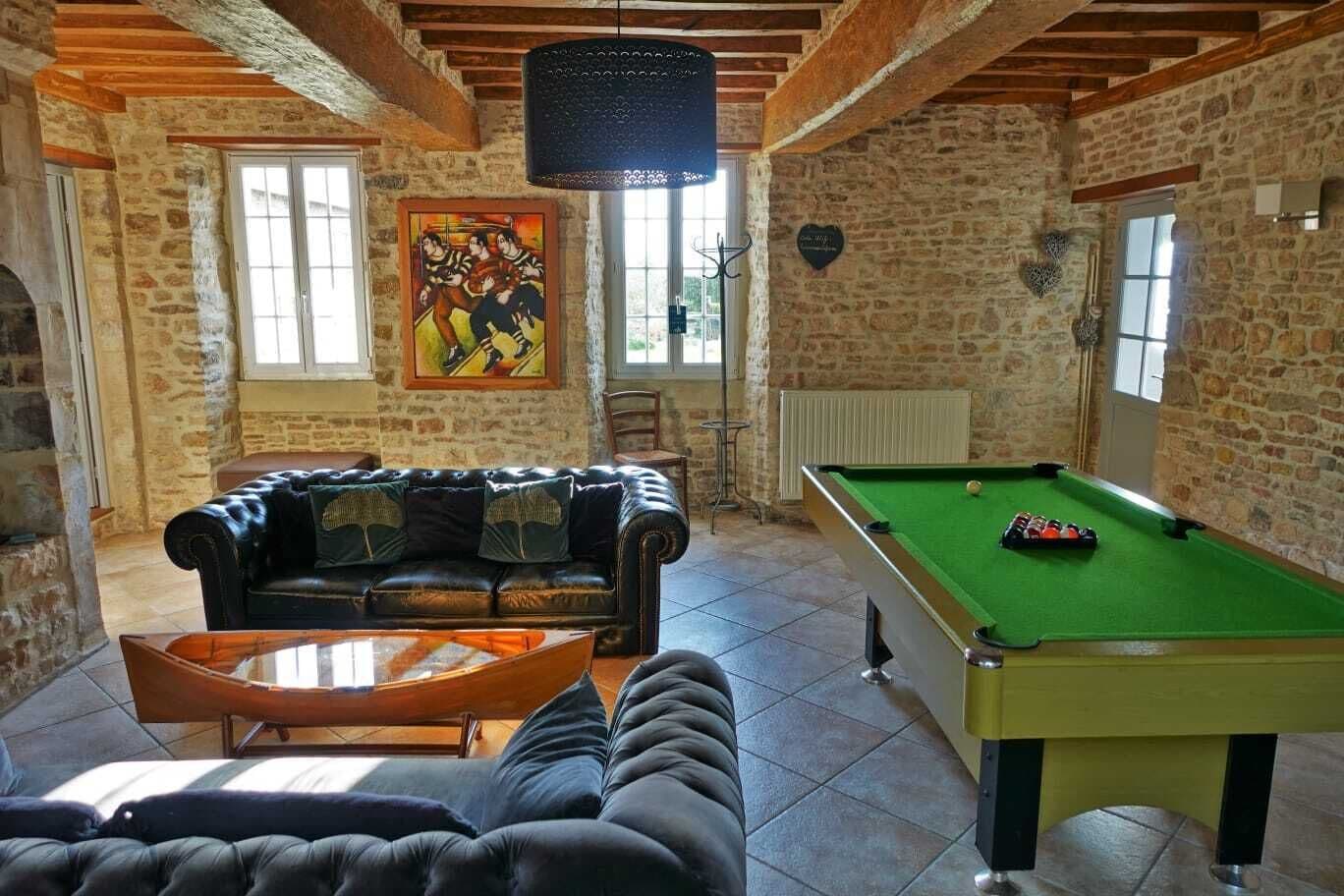 Une pièce chaleureuse avec une table de billard, un canapé en cuir et un porte-queue de billard.