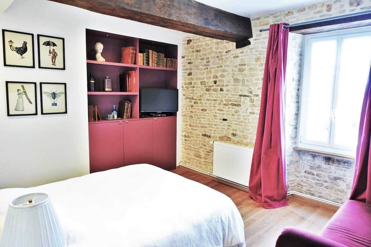 Een slaapkamer met een bed, een boekenkast, een televisie en een stenen muur.