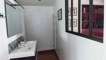 Um corredor estreito com uma porta, um radiador e uma pia brancos, além de um espelho.