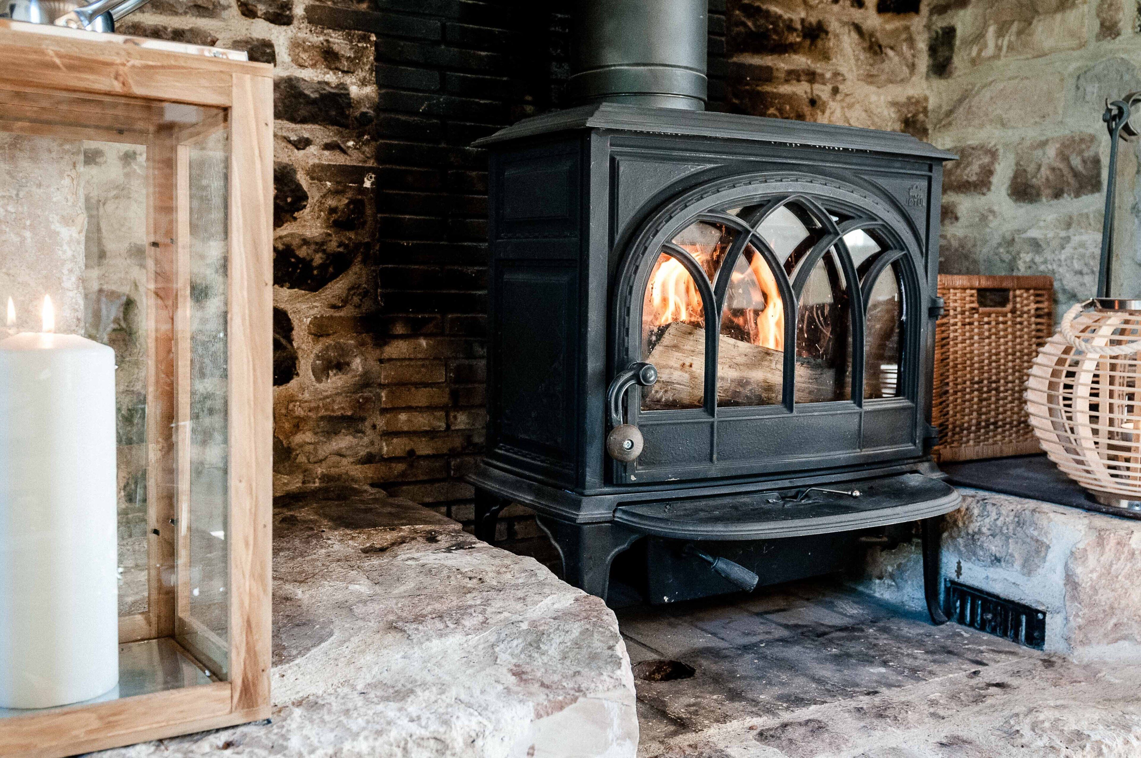 A stone fireplace with a black wood-burning stove, a lit candle, and a wicker basket.