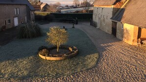 A courtyard with a central tree, stone walls, and buildings with sloped roofs. - La Ferme D'ervée de Saint-Roch (Isigny-sur-Mer)