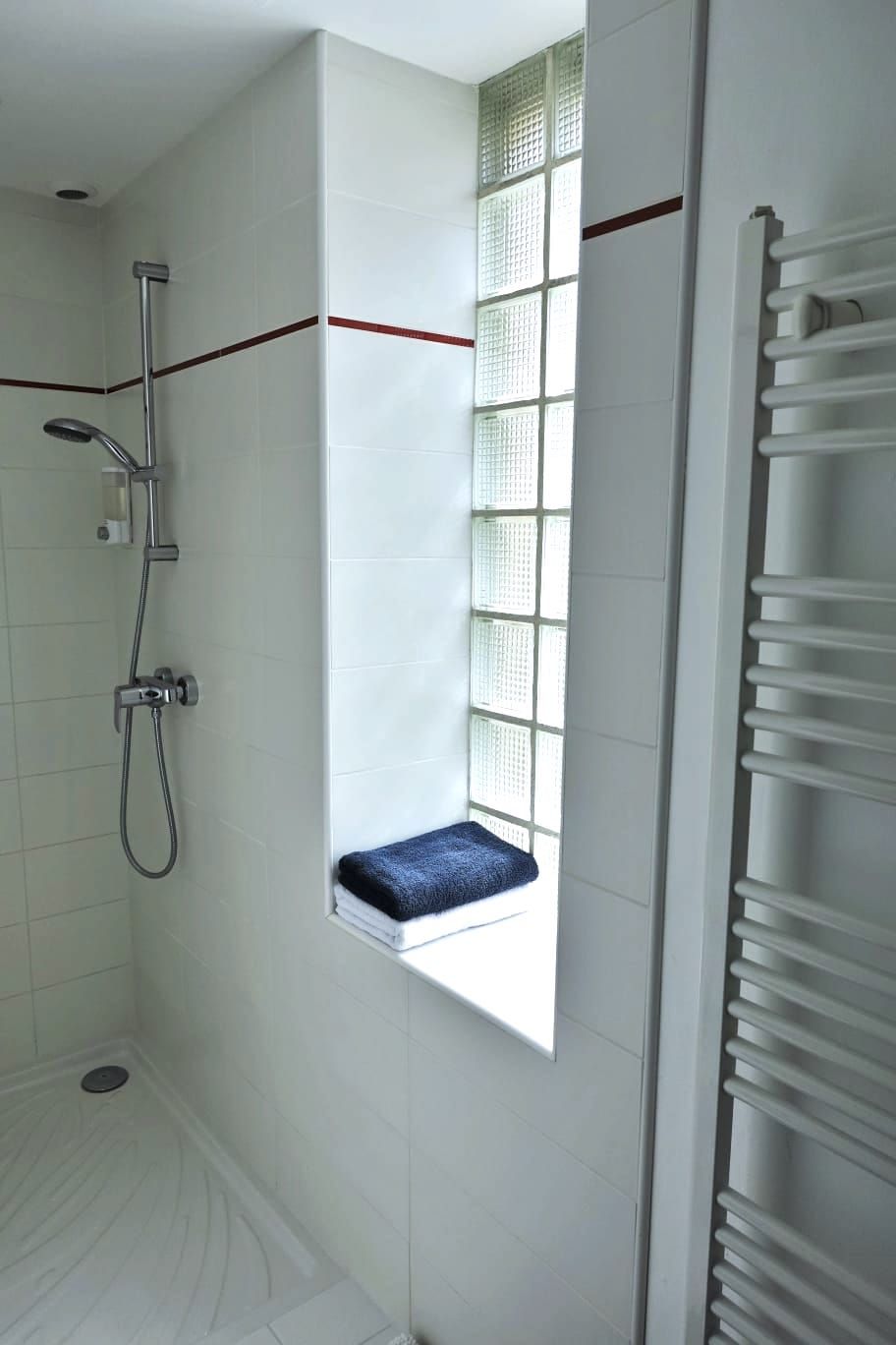 Une salle de bain avec une douche, une fenêtre avec une serviette et un radiateur.