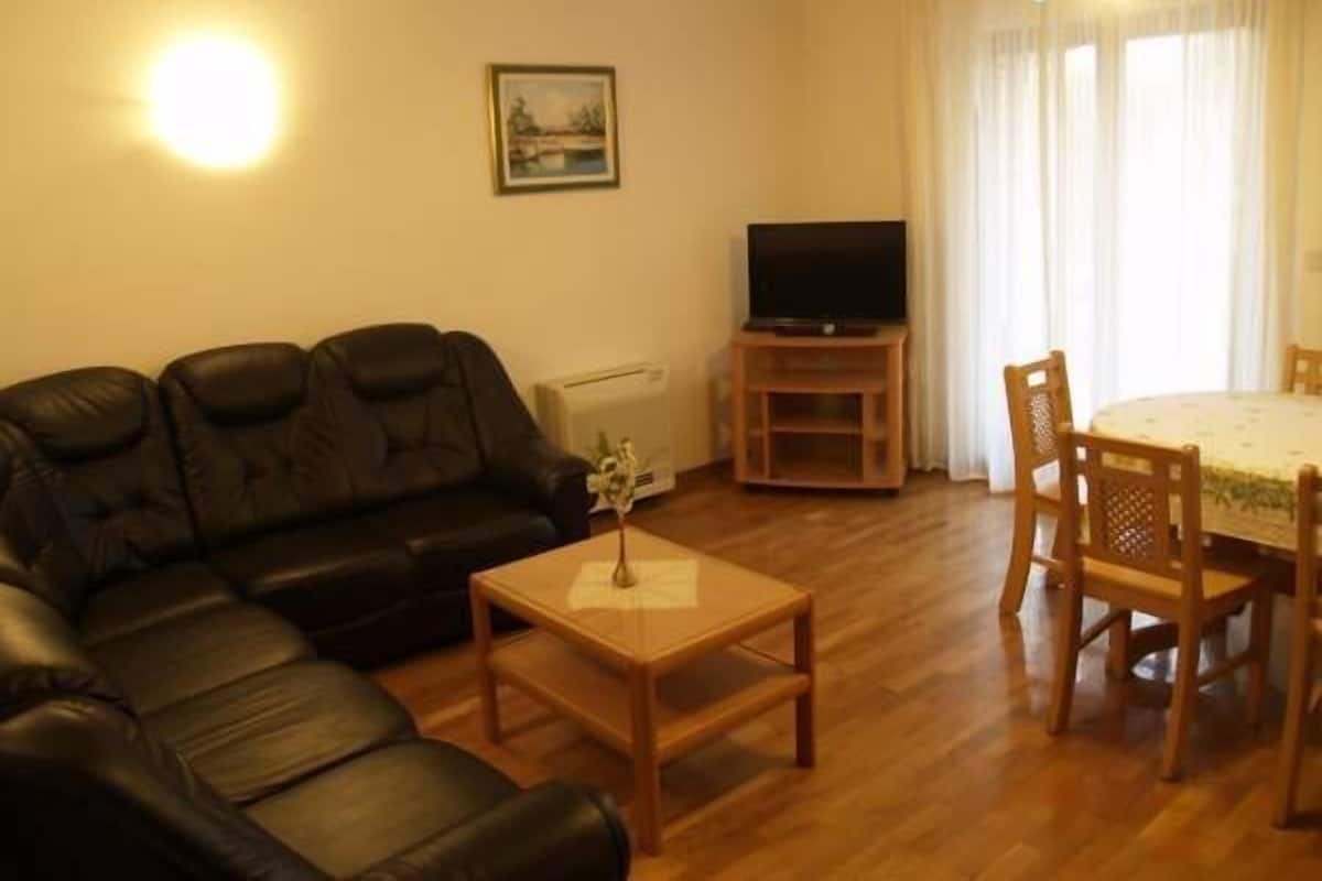 Un salon avec un canapé en cuir noir, une table basse en bois, un téléviseur posé sur un meuble et une table à manger avec des chaises.