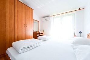 Un dormitorio con un armario de madera, un escritorio y una cama con ropa de cama blanca.