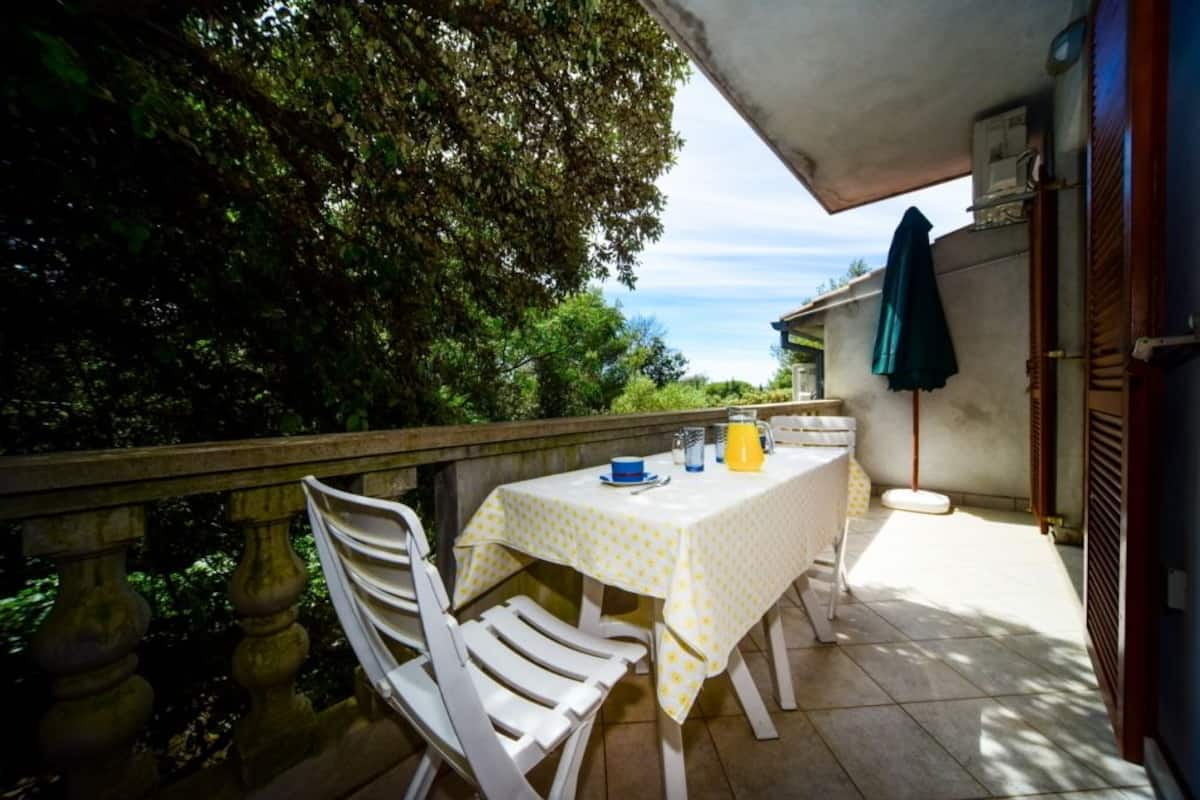 Un balcon avec une table dressée pour deux personnes, des chaises et une vue sur la mer.