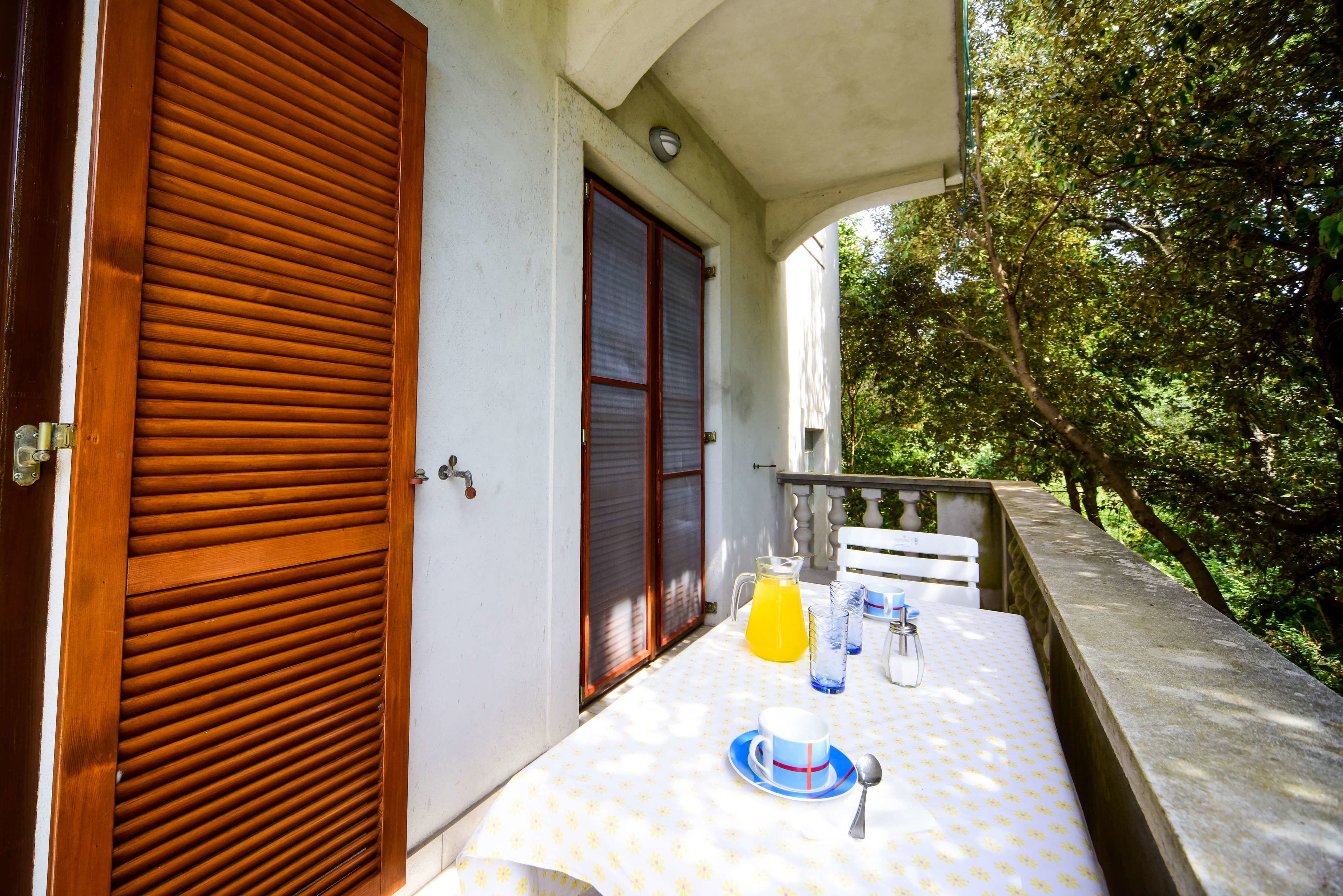 Un balcon avec une table mise pour le petit-déjeuner, comprenant une carafe de jus d’orange, des tasses et une cuillère.