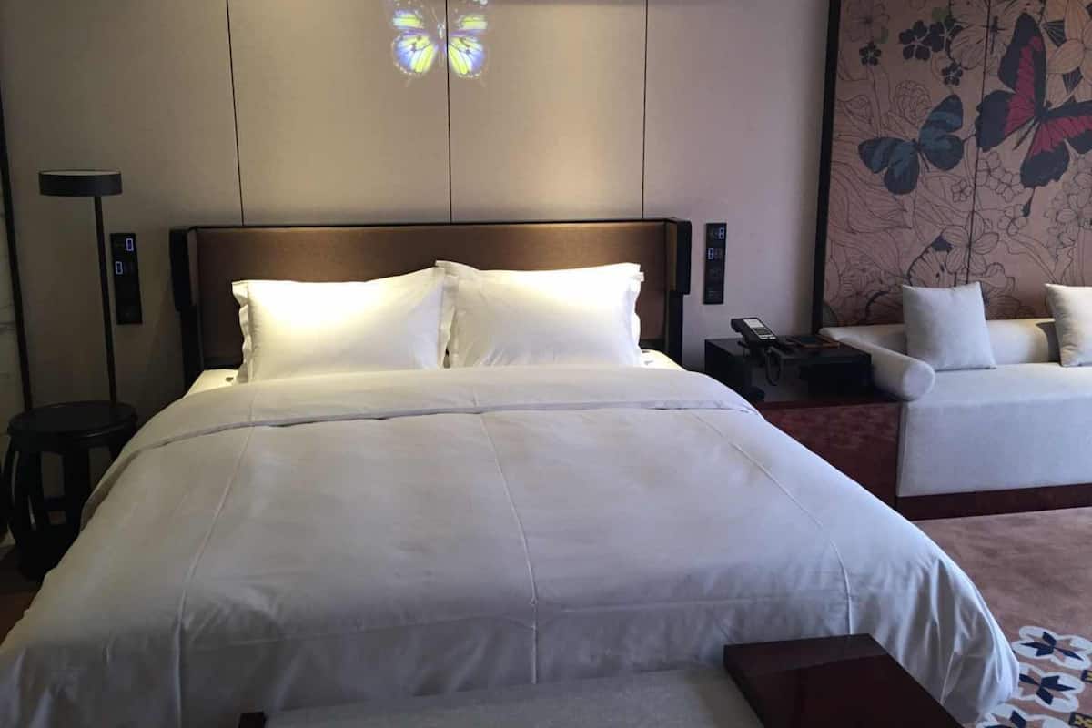 Una habitación de hotel con una cama grande, una mesita de noche con lámpara, una pequeña mesa y un sofá.
