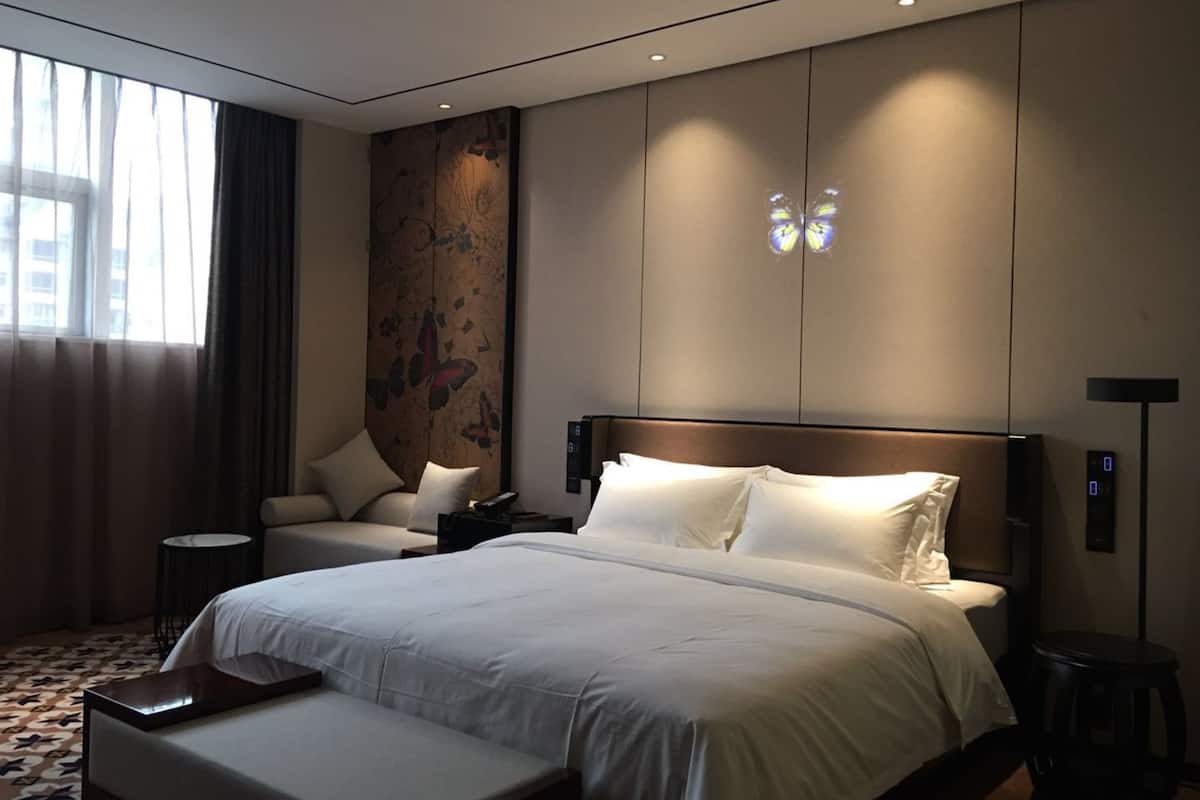Habitación de hotel moderna con una cama grande, un escritorio, una silla y un ventanal amplio.