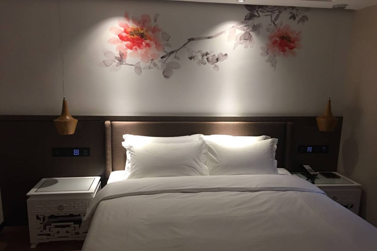 Habitación de hotel con una cama grande, dos mesitas de noche, un reloj en la pared y un adorno floral en la pared.