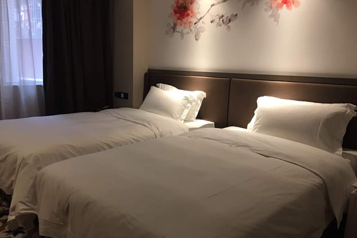 Habitación de hotel con dos camas, cabecera y una pared decorada con motivos florales.