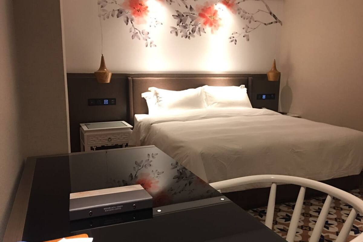 Una habitación de hotel con una cama, mesitas de noche, un escritorio con una computadora y un adorno en la pared.