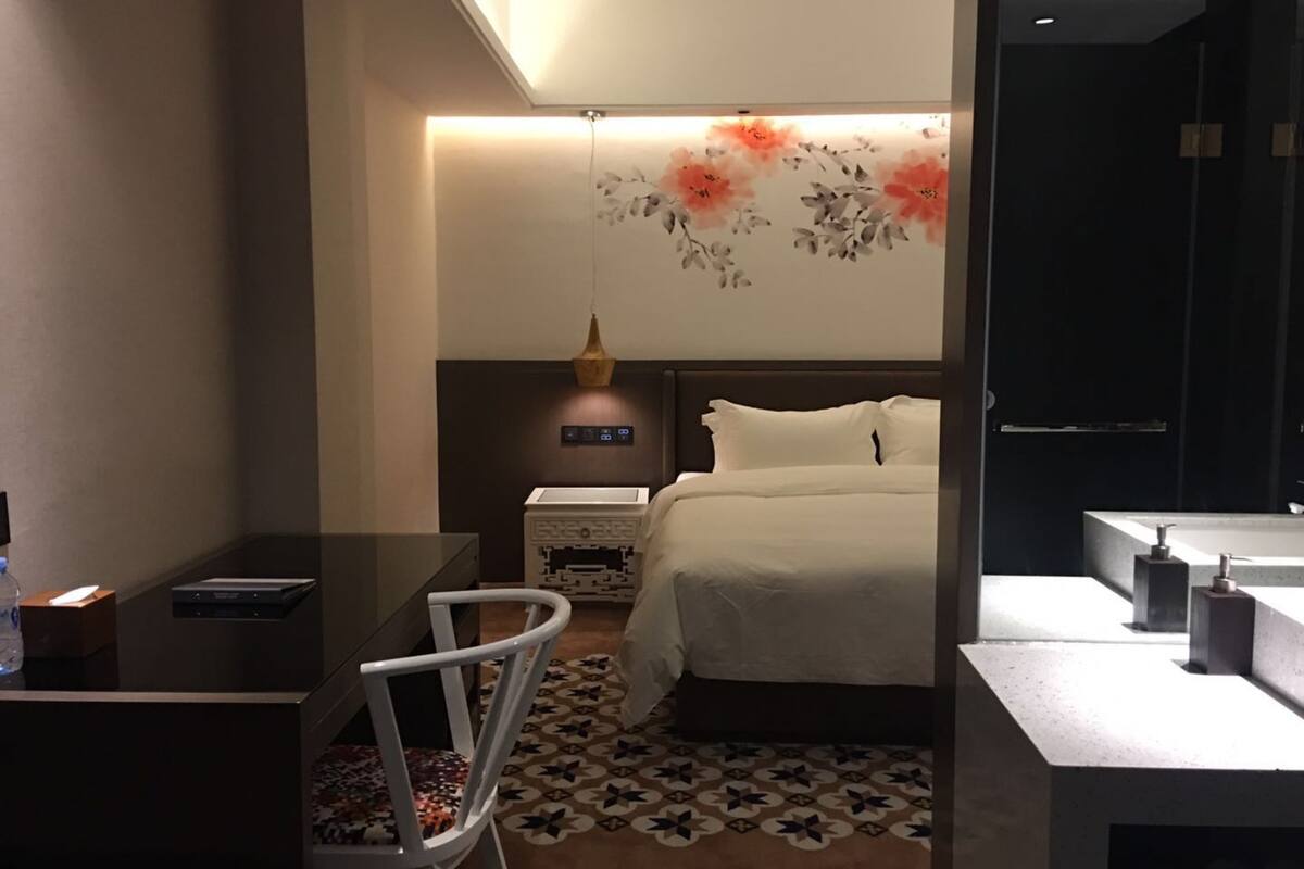 Una habitación de hotel moderna con cama, escritorio, silla, mesita de noche y zona de baño.