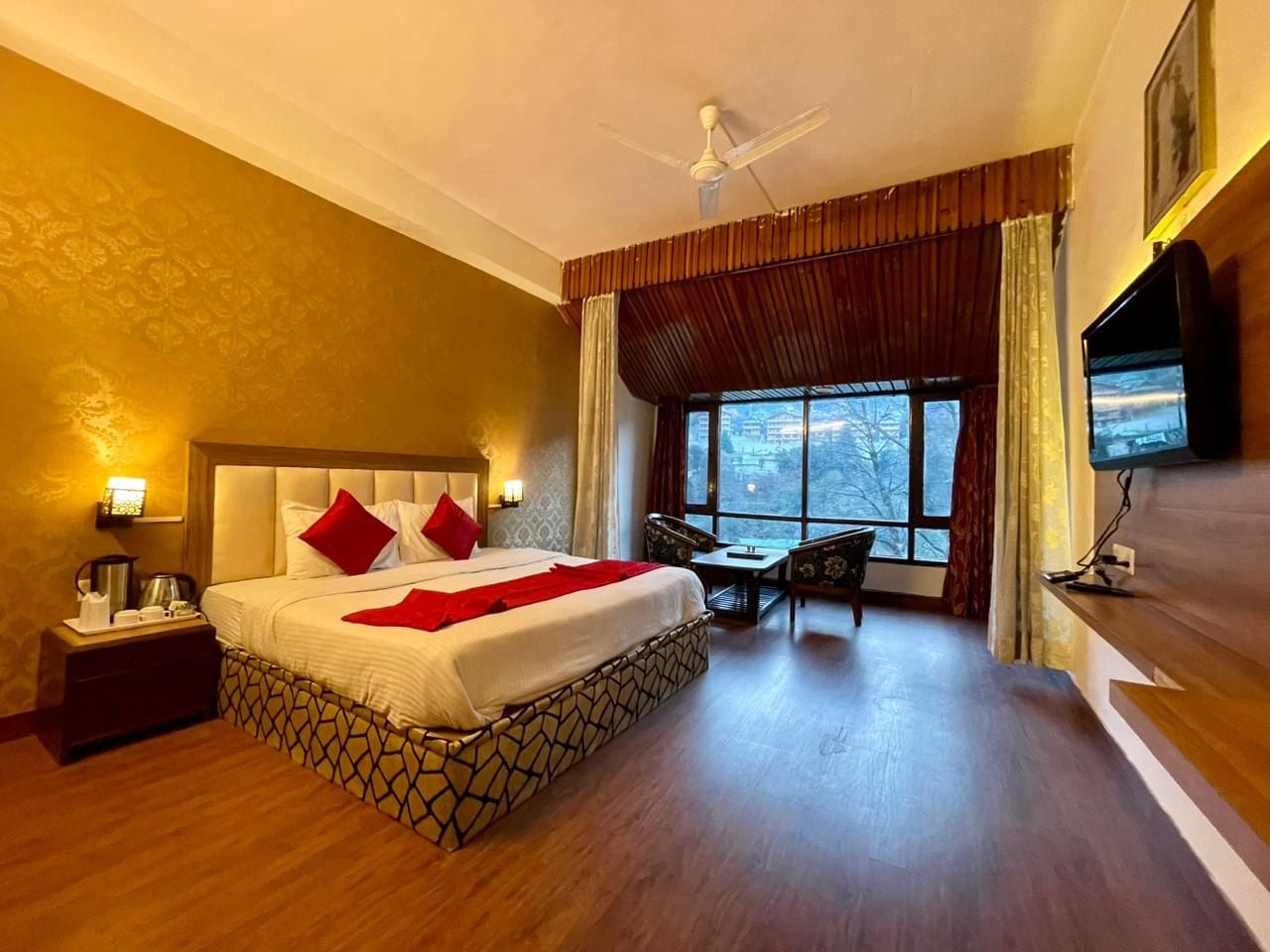 A hotel room with a large bed, a desk, a chair, a television, and a window with a view.