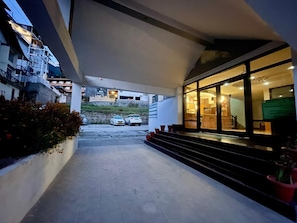 A building with a covered walkway leading to a brightly lit entrance. - Hotel Sitara international (Manali)