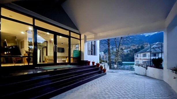 A modern building with a covered outdoor area, steps leading to a glass entrance, and a view of mountains in the background. - Hotel Sitara international (Manali)