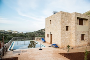 A stone building with a swimming pool and lounge chairs. - Uphoria Stone Villas (Mylopotamos)