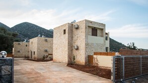 A stone building with multiple rooms, a paved driveway, and a mountainous backdrop. - Uphoria Stone Villas (Mylopotamos)