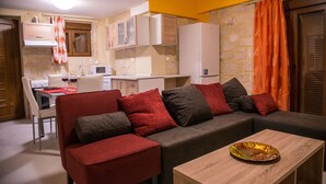 A compact living space with a sofa, a dining table, and a kitchen area. - Uphoria Stone Villas (Mylopotamos)