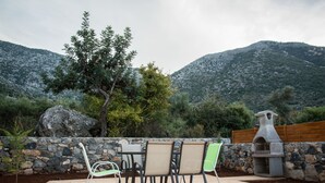 An outdoor patio with stone walls, a stone barbecue, and a view of mountains. - Uphoria Stone Villas (Mylopotamos)