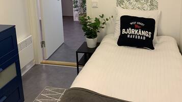 Une chambre à coucher avec un lit, une table de chevet ornée d’une plante, une commode bleue et une porte donnant sur une autre pièce.