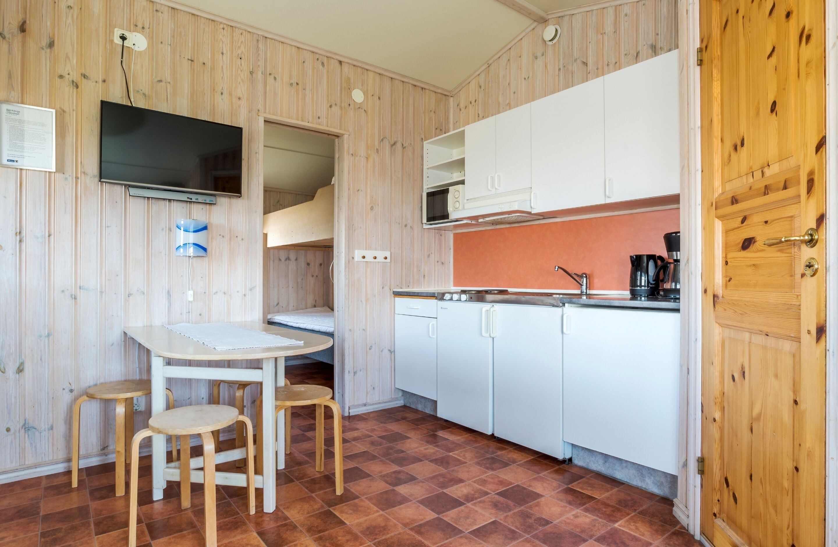 Une cuisine de taille réduite avec un revêtement mural en bois, un plan de travail blanc et un four à micro-ondes encastré.