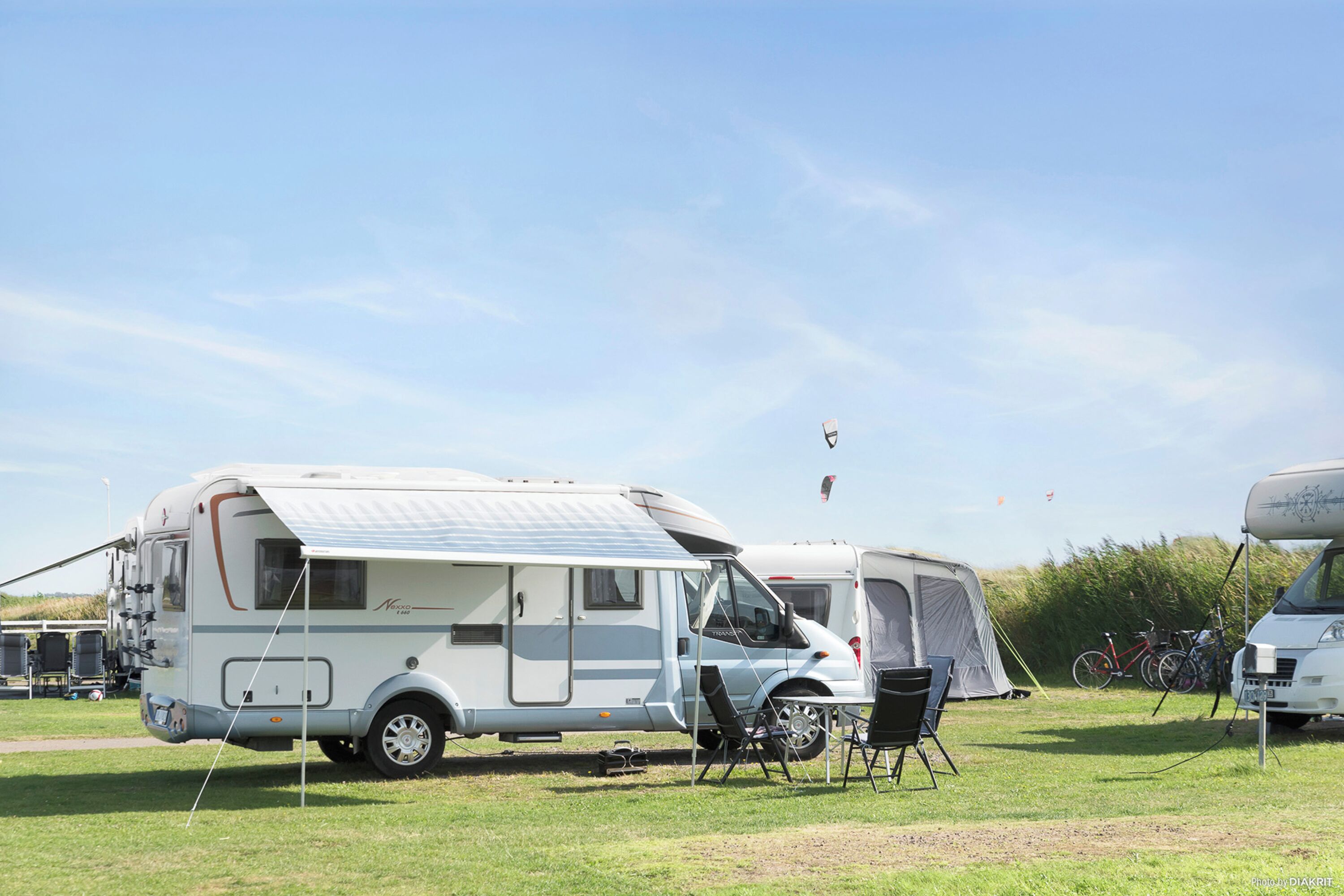 Een caravan met een afgedekte zijkant, een kleine aanhanger, een tent en een fiets in een grasveld.