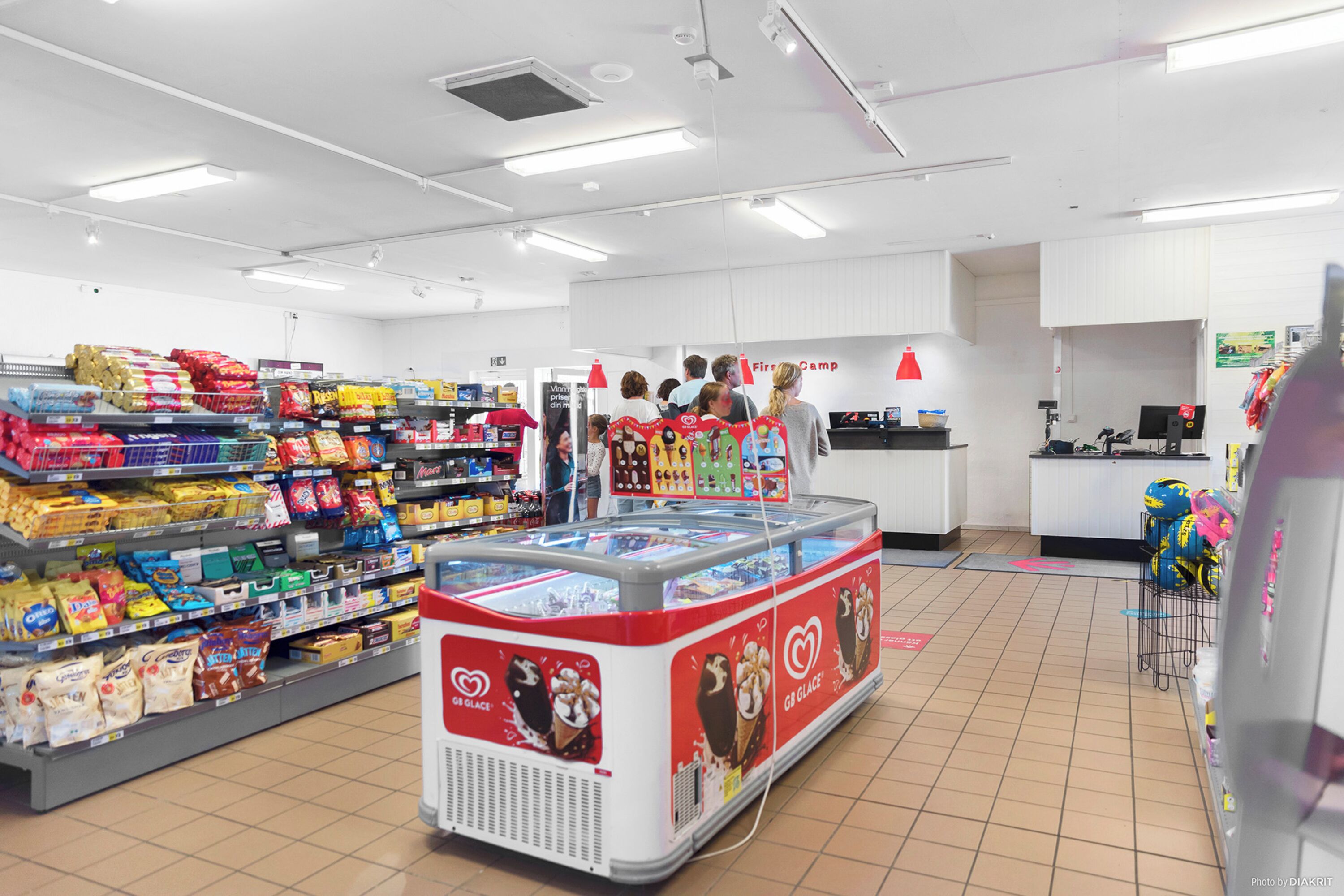 A grocery store with shelves stocked with various products, a freezer display, and a checkout counter.