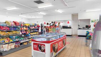 A grocery store with shelves stocked with various products, a freezer display, and a checkout counter.