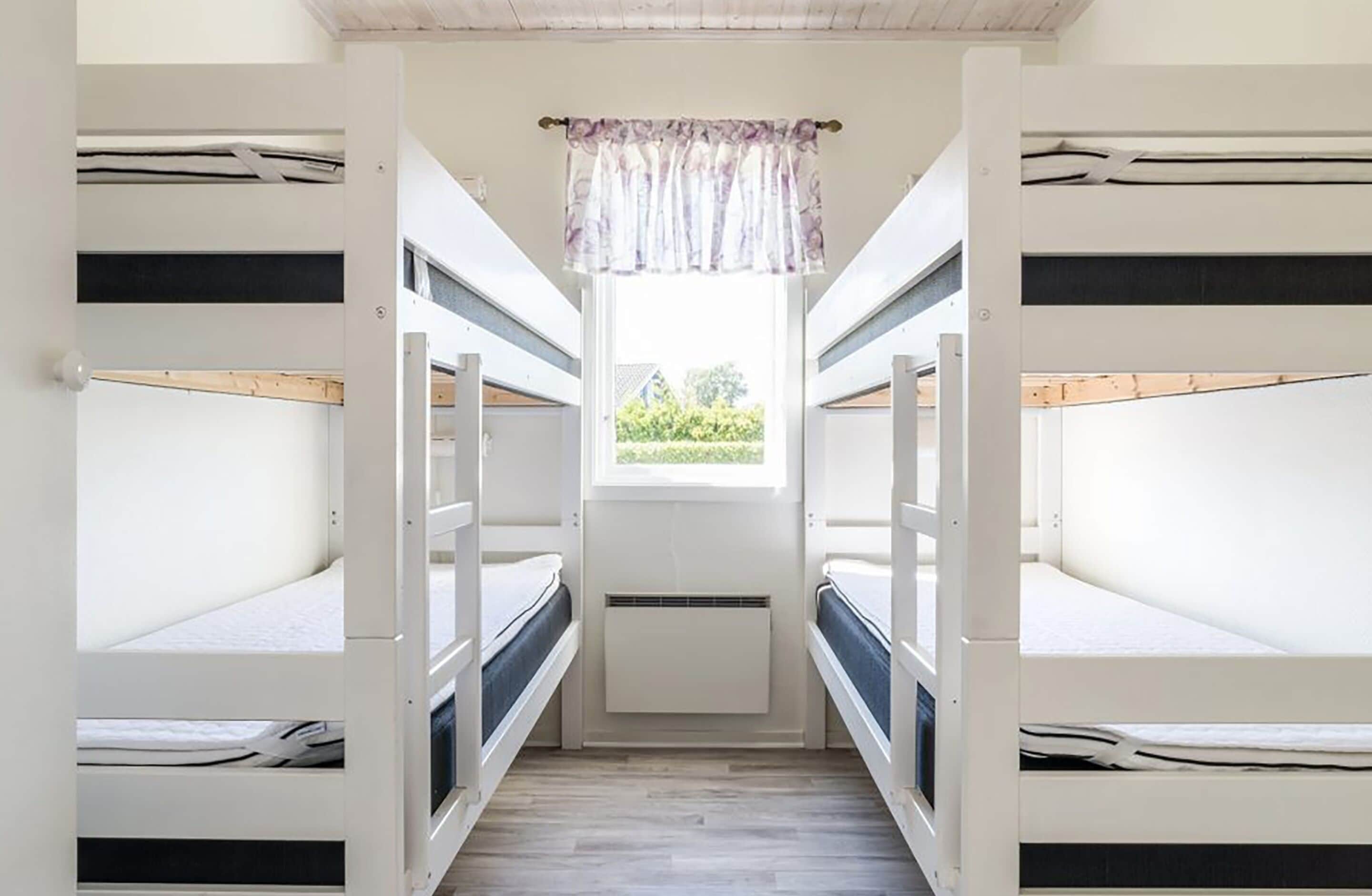 A narrow room with bunk beds, a window with a curtain, and a radiator.