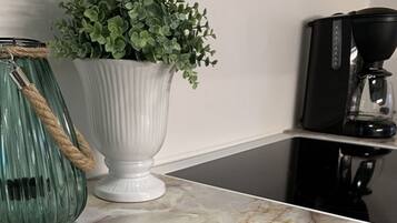 A kitchen counter with a white vase containing green foliage, a green glass jar with a rope, and a black coffee maker.