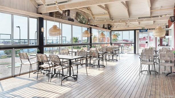 Un espace de restauration intérieur avec des tables et des chaises en bois, de grandes fenêtres et des luminaires suspendus.