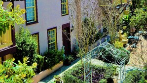 A two-story house with a sloped roof, multiple windows, and a garden with various plants and a small fountain. - Casa De Solana Bed & Breakfast (St. Augustine)
