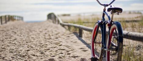 Een fiets geparkeerd op een zandpad met een houten hek en uitzicht op het strand.