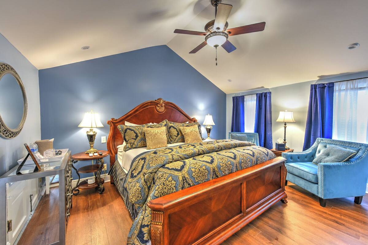 Une chambre avec un grand lit, deux tables de chevet, un ventilateur de plafond et un fauteuil bleu.