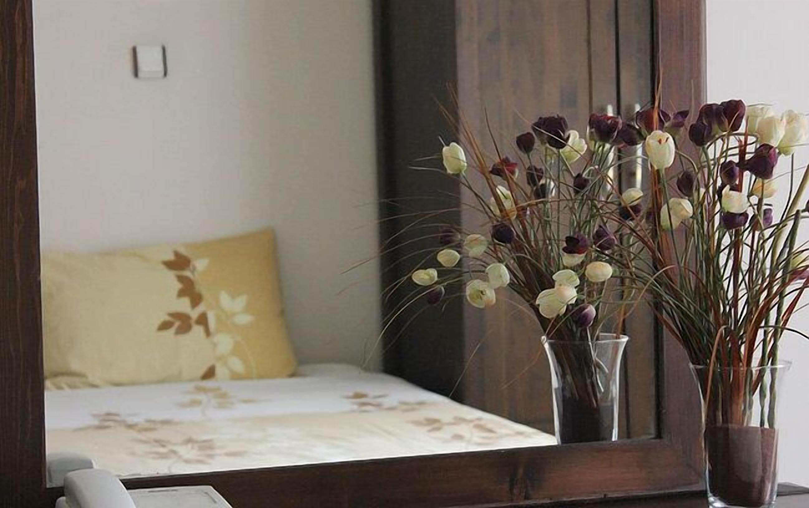 Un dormitorio con una cama, un espejo y dos jarrones con flores.